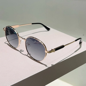 Close-up of retro round gold metal sunglasses with dark grey gradient lenses on a pedestal