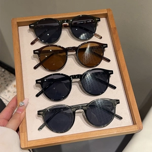 Close-up of four classic round sunglasses with metal rivet details in a wooden tray