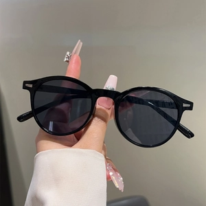Close-up of black round frame sunglasses with silver rivet accents held by hand