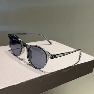 Detail of translucent gray round sunglasses with silver rivets on a light pink stand