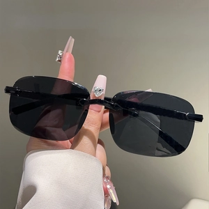 Gros plan de lunettes de soleil carrées sans monture tenues par une main décorée