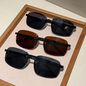 Trois lunettes de soleil carrées sans monture noires et marron sur un plateau en bois