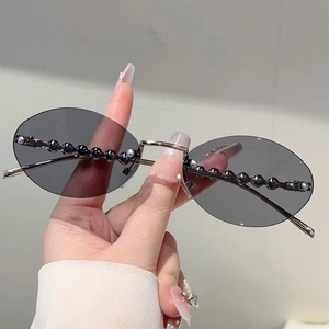 Close-up of rimless oval sunglasses with dark grey lenses and pearl bead trim details