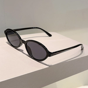 Vue détaillée de lunettes de soleil ovales noires sur un support minimaliste gris poli