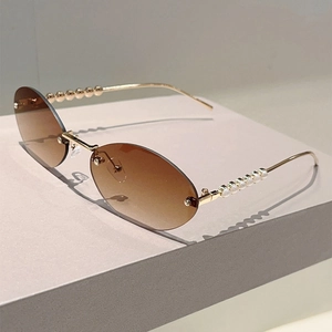 Detail of gradient tea lenses and gold metal temples with pearl accents on oval sunglasses