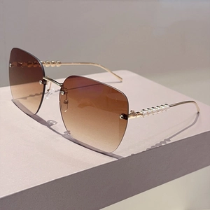 Détail de lunettes de soleil carrées sans monture avec dégradé brun et branches dorées perlées