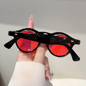 Close-up of retro round sunglasses with red lenses and gold rivet accents on black frame