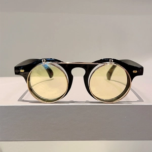 Vintage punk flip-up round sunglasses with black frames and yellow lenses on a grey stand