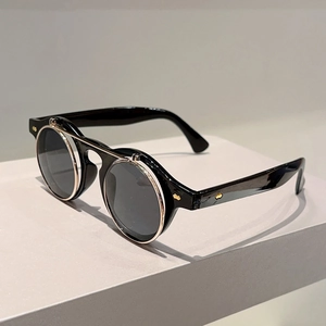Detail of round flip-up sunglasses with black frames and gold metal hinges on grey surface