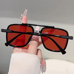 Detail of square oversized sunglasses with orange lenses and textured black temples