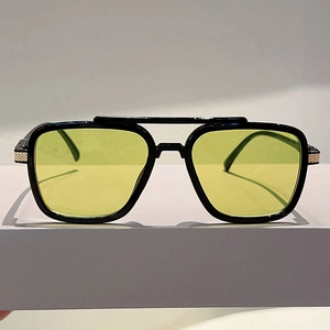 Detail of oversized black square sunglasses with yellow-green lenses and golden metal accents