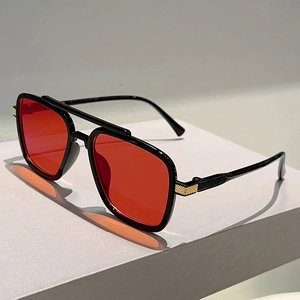Detail view of red lenses and golden metal mesh on black double bridge sunglasses