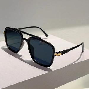 Detailed close-up of square black sunglasses with golden metal accents and grey lenses