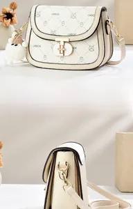 Detail of off-white saddle bag with lychee texture, golden twist lock and plush charm