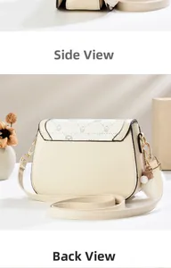 Detail view of cream-colored saddle bag showing side profile and plush pompom charm