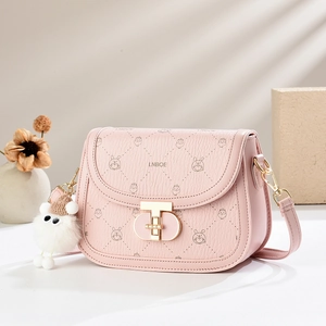 Pink saddle bag with cartoon patterns, gold rotary lock, and plush bear charm in soft lighting