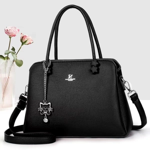 Detail of black pebbled leather handbag with silver logo and cat charm on gray background