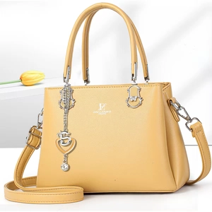 Close-up of mustard yellow leather handbag featuring silver hardware and a heart charm