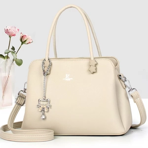 Detail of beige pebbled leather handbag with metal cat charm and adjustable strap