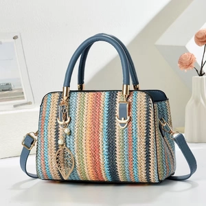 Colorful woven crossbody bag with blue leather handles and a gold leaf pendant detail
