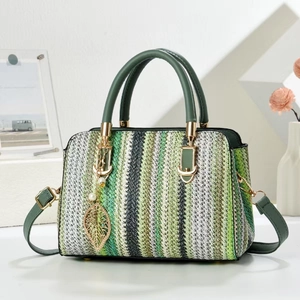 Green and white woven crossbody bag with pearl leaf charm and top handle on white surface