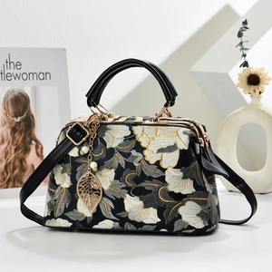 Detail of floral embroidery on a vintage handbag with a gold leaf pendant and pearl decor
