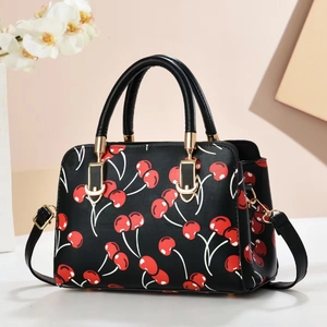 Close-up of black leather crossbody bag featuring red cherry prints and gold hardware