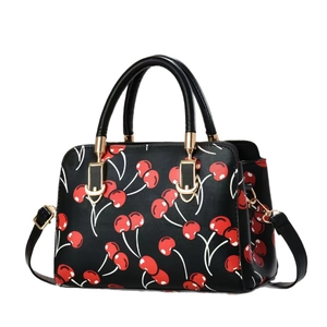 Minimalist black boston handbag with red cherry print and golden hardware on white background