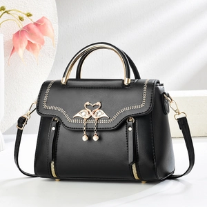 Elegant black leather handbag with gold handle and swan pearl pendant on a white podium