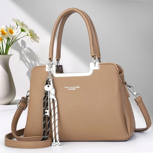 Detail of tan pebble leather tote bag with silver metal bar handle and cord charm