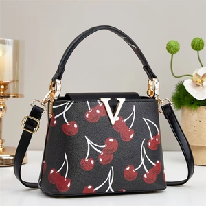 Close-up of black leather bucket bag with red cherry print and gold V-shaped logo buckle