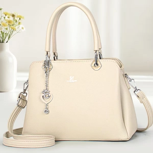 Detail of elegant beige crossbody bag showing litchi grain texture and silver heart pendant