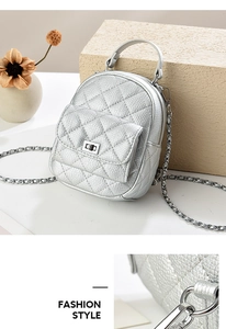 Detail of silver quilted mini backpack with metallic chain and turn-lock on stone surface