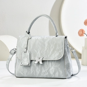 Detail of grey wrinkled glossy bag with butterfly buckle and metal floral pendant