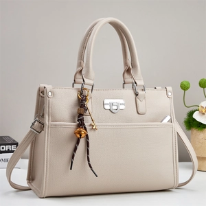 Detail of beige lychee leather handbag with silver lock and decorative charms