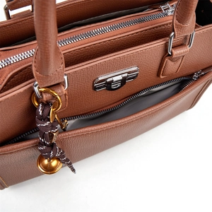 Close-up of brown litchi pattern leather handbag with multi-layer zippers and bell charm