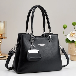 Detail of black litchi leather tote bag with elegant logo and mini charm accessory
