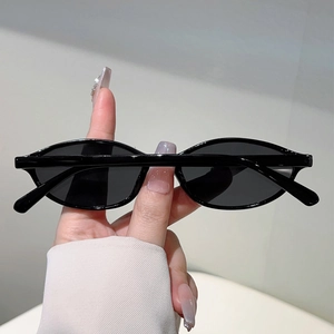 Detail view of glossy black oval sunglasses with dark lenses held in hand for fashion