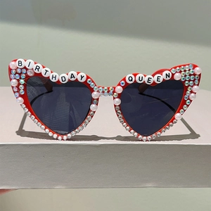 Vue détaillée des lunettes de soleil cœur rouges avec perles, strass et texte Birthday Queen