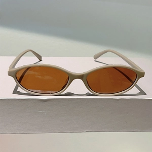 Close-up of retro oval frame sunglasses in beige with tinted brown lenses on a stand