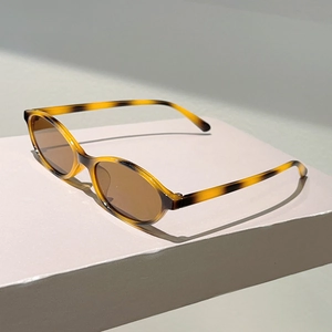 Close-up of retro oval tortoise shell sunglasses with brown lenses on a beige stand