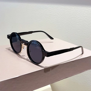 Retro round black frame sunglasses with golden metal bridge on a pink geometric stand