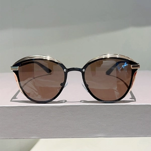 Detail of cat-eye sunglasses featuring black frame with gold metal trim and brown lenses
