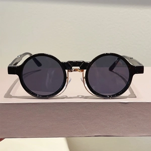 Detailed close-up of retro round sunglasses with black frames and gold bridge on a stand