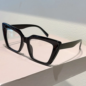 Close-up of black oversized cat-eye glasses frames on a pink display pedestal
