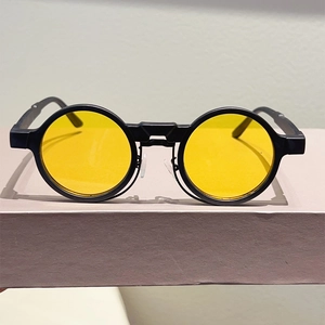 Close-up of matte black round frame sunglasses with vibrant yellow lenses and nose pads