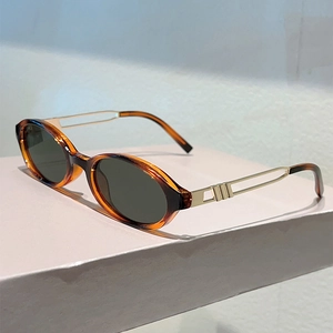 Detail view of oval tortoiseshell sunglasses with golden hollow metal temples on a stand