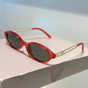 Detail of red oval sunglasses featuring hollowed golden metal temples and UV lenses