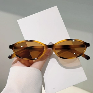 Retro tortoise shell oval sunglasses with brown tinted lenses held against white card