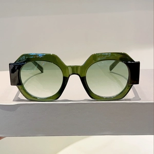 Close-up of thick dark green geometric sunglasses with gradient lenses on a pedestal